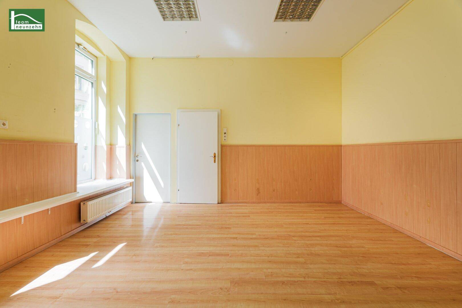 Geräumiger, heller Raum mit Laminatboden und Holzpaneelen, mit zwei Türen.