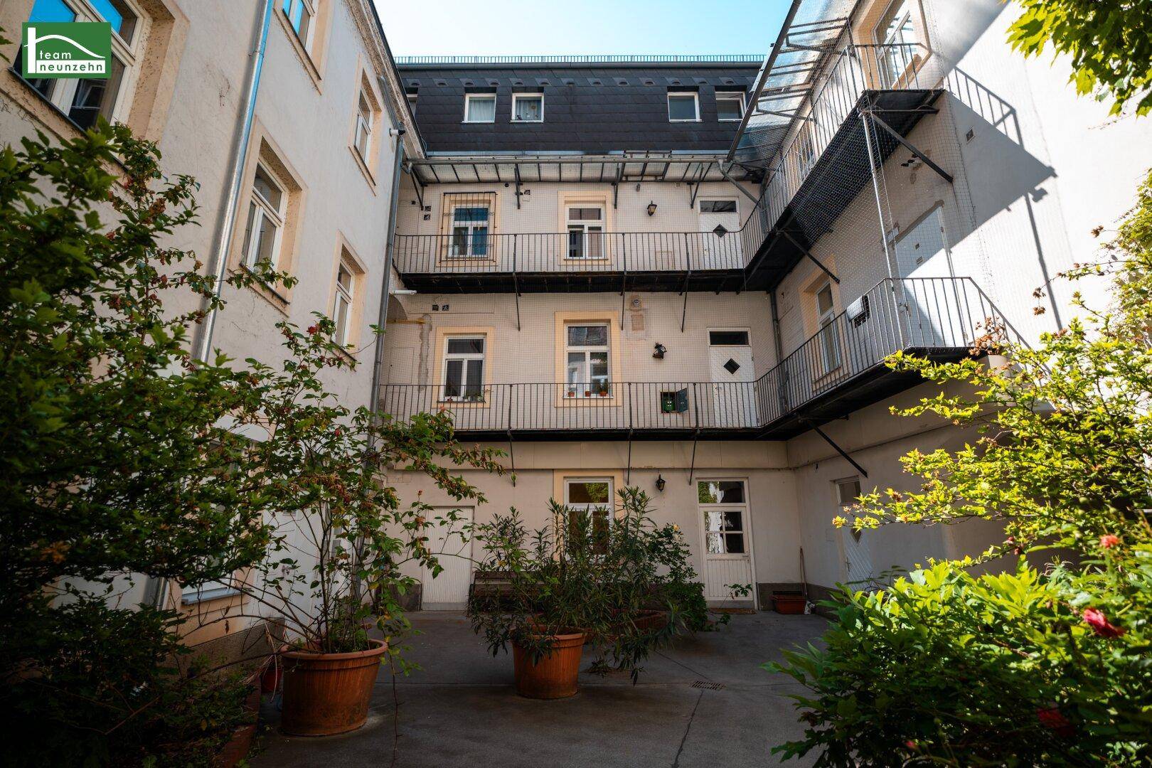Innenhof eines Gebäudes mit Pflanzen in Töpfen und Außentreppen zu den Balkonen.