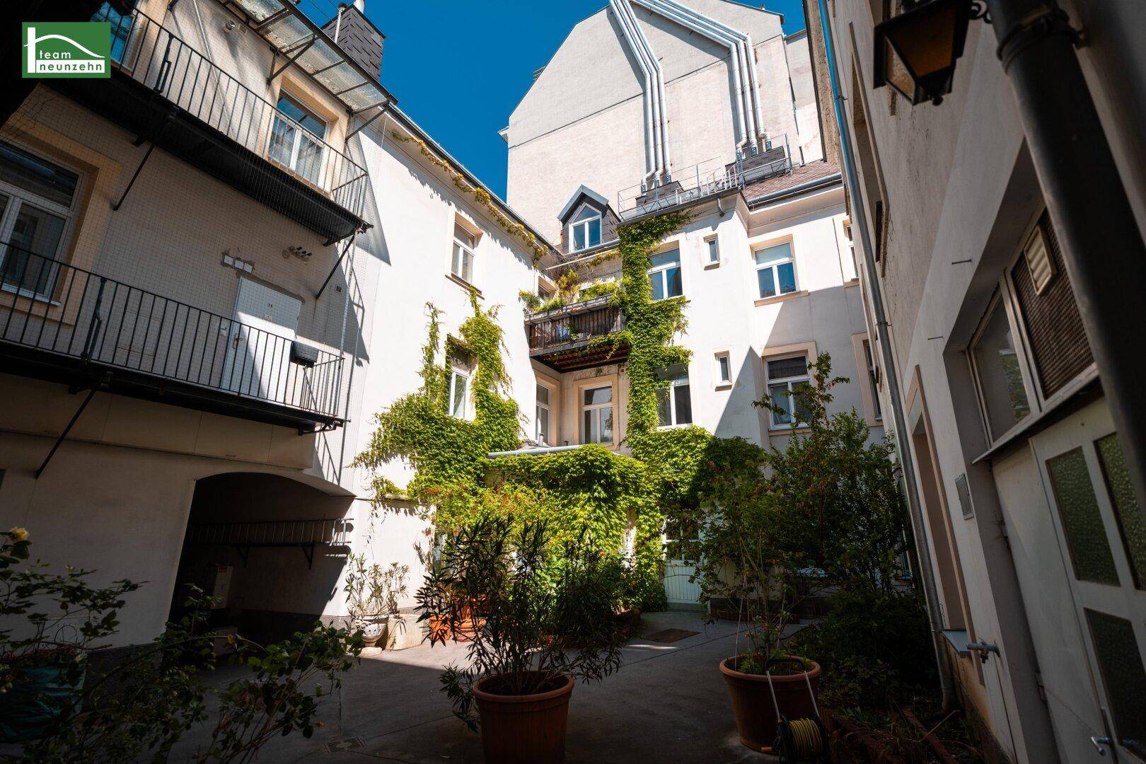 Begrünter Innenhof mit Kletterpflanzen an der Fassade und Zugang zu weiteren Gebäudeteilen.