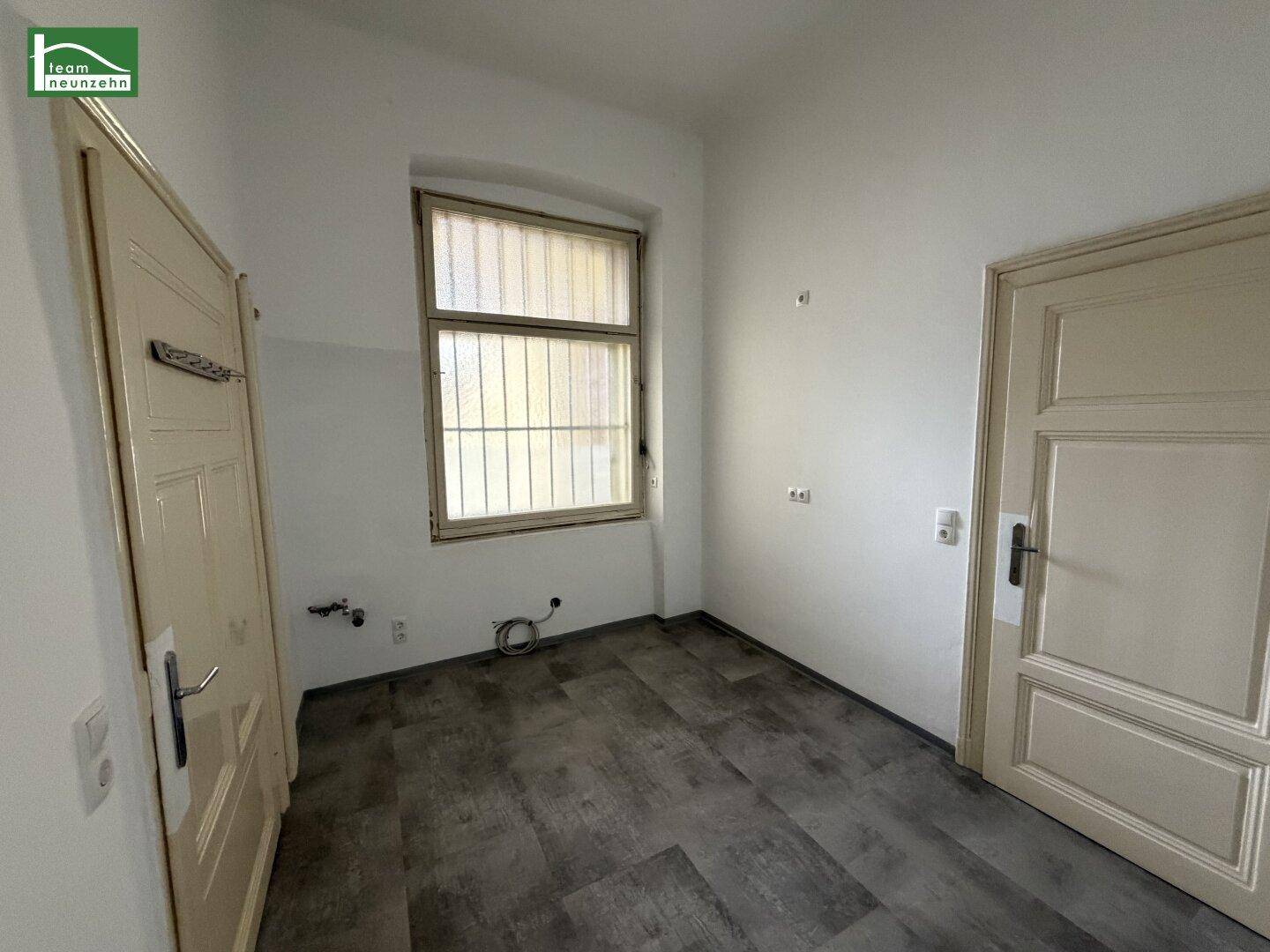 Leere Küche mit dunklem Vinylboden und Anschlussmöglichkeiten für eine Einbauküche.