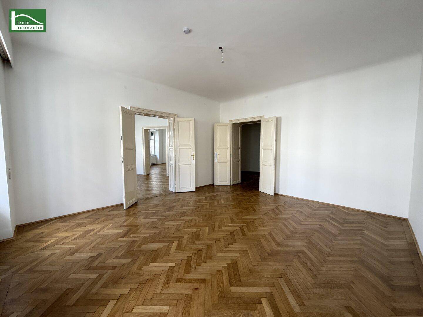 Geräumiges, leeres Zimmer mit Fischgrätparkett und hohen Türen, ideal für Wohnzwecke.