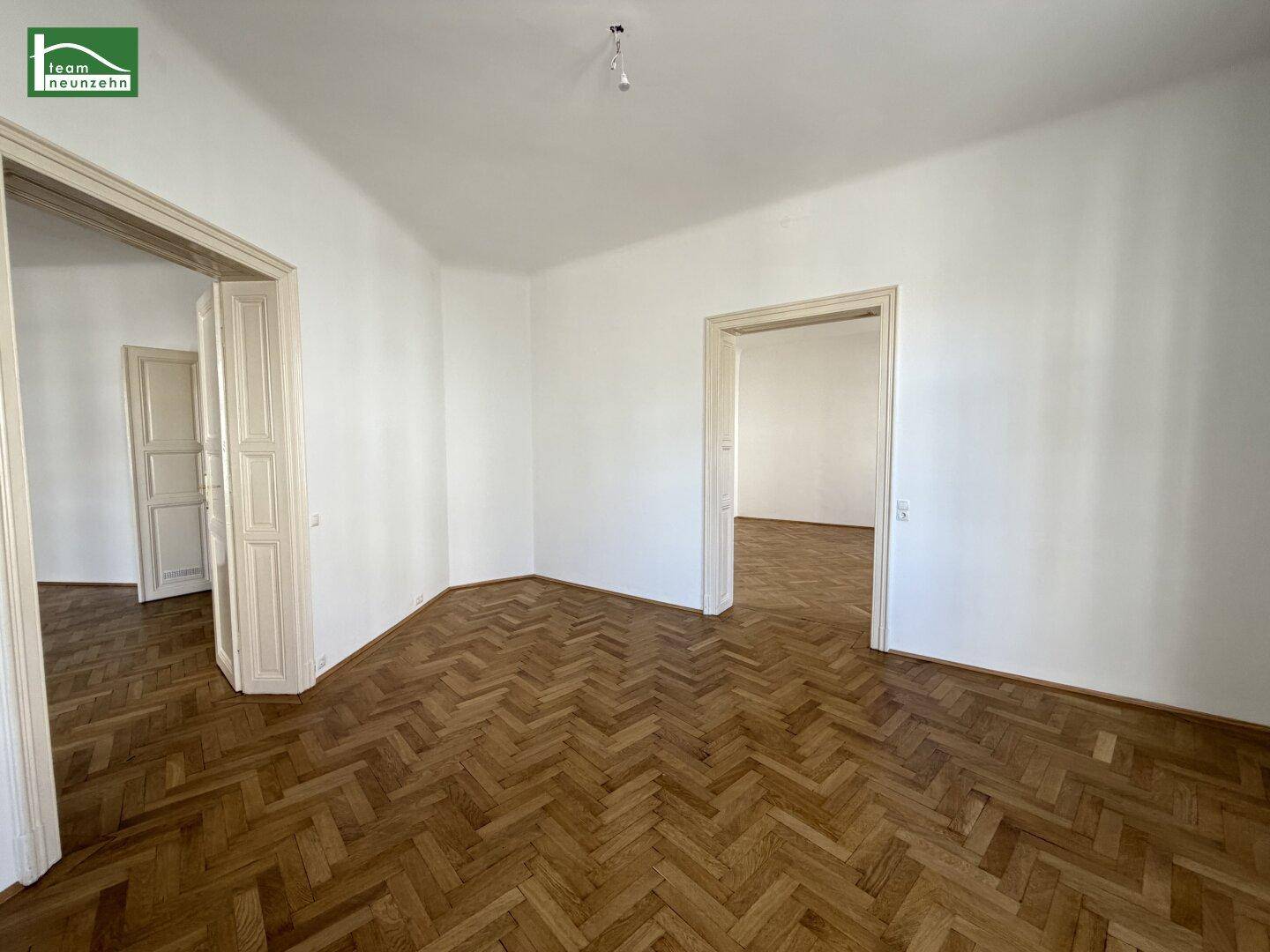 Heller Flur mit Fischgrätparkett und hohen Türen, der zu verschiedenen Räumen führt.