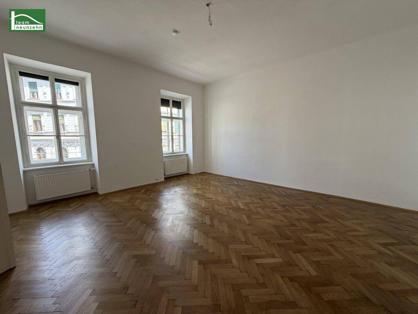 Geräumiges, leeres Zimmer mit Fischgrätparkett und hohen Fenstern, bereit zur individuellen Gestaltung.