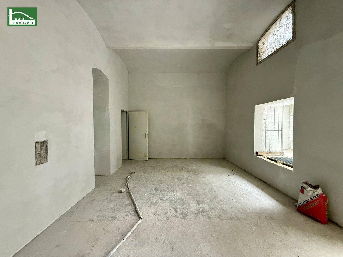 Leerer Raum mit glatten grauen Wänden, einem Fenster und Betonboden, bereit für den Ausbau.