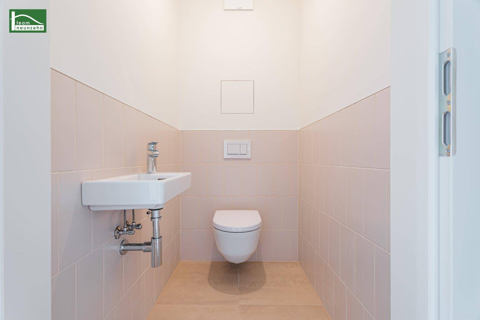 Kleines Gäste-WC mit wandhängender Toilette und Waschbecken in hellen Fliesen.