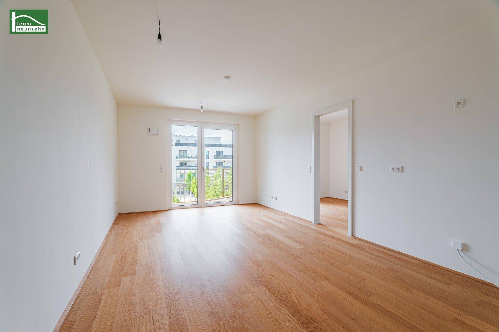 Helles, leeres Zimmer mit Holzboden und Zugang zu einem Balkon.