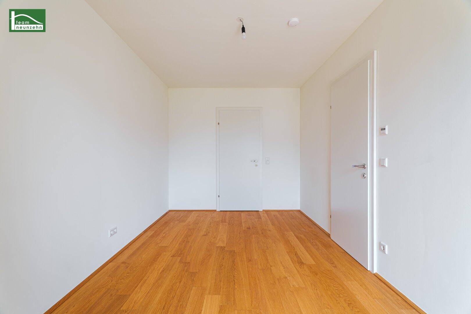 Helles, leeres Zimmer mit Holzboden und zwei weißen Türen.