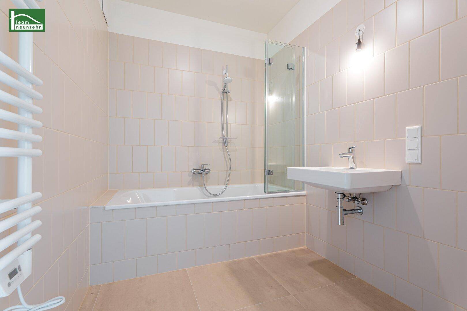 Helles Badezimmer mit Badewanne, Duschwand, Waschbecken und beheiztem Handtuchhalter.