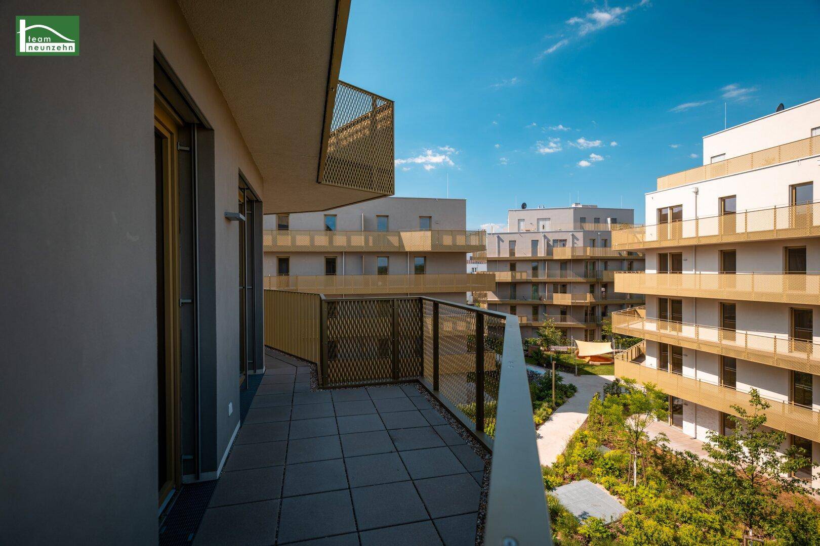 Geräumiger Balkon mit Fliesenboden und Blick auf die moderne Wohnanlage und den begrünten Innenhof.