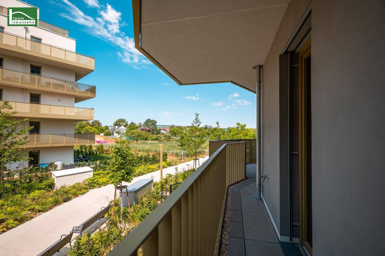 Langer Balkon mit Fliesenboden und weitem Blick über die grüne Umgebung und Wohngebäude.