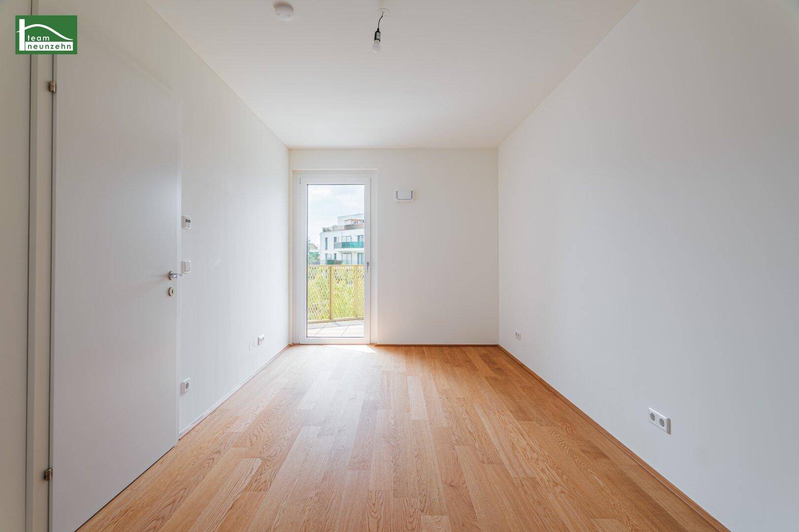 Leeres Zimmer mit Holzboden und Zugang zu einem kleinen Balkon oder Austrittsbereich.