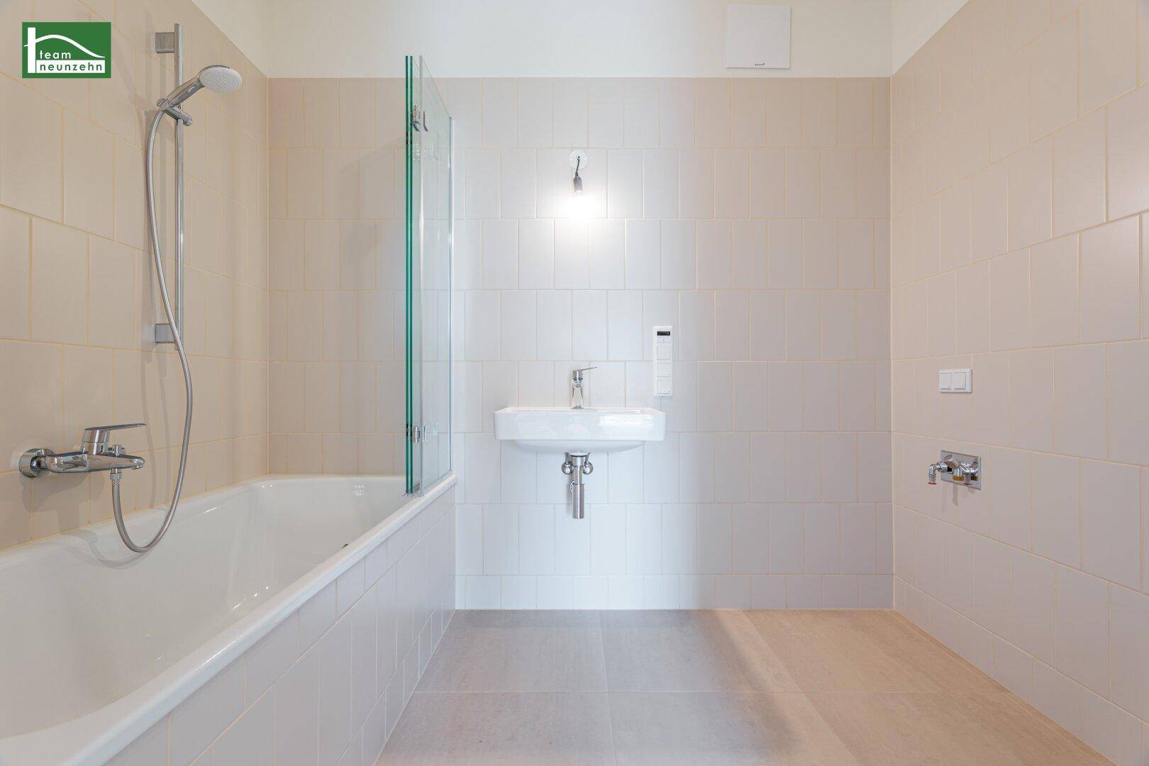 Modernes Badezimmer mit Badewanne, Duschabtrennung und hellen Fliesen in neutralen Farben.