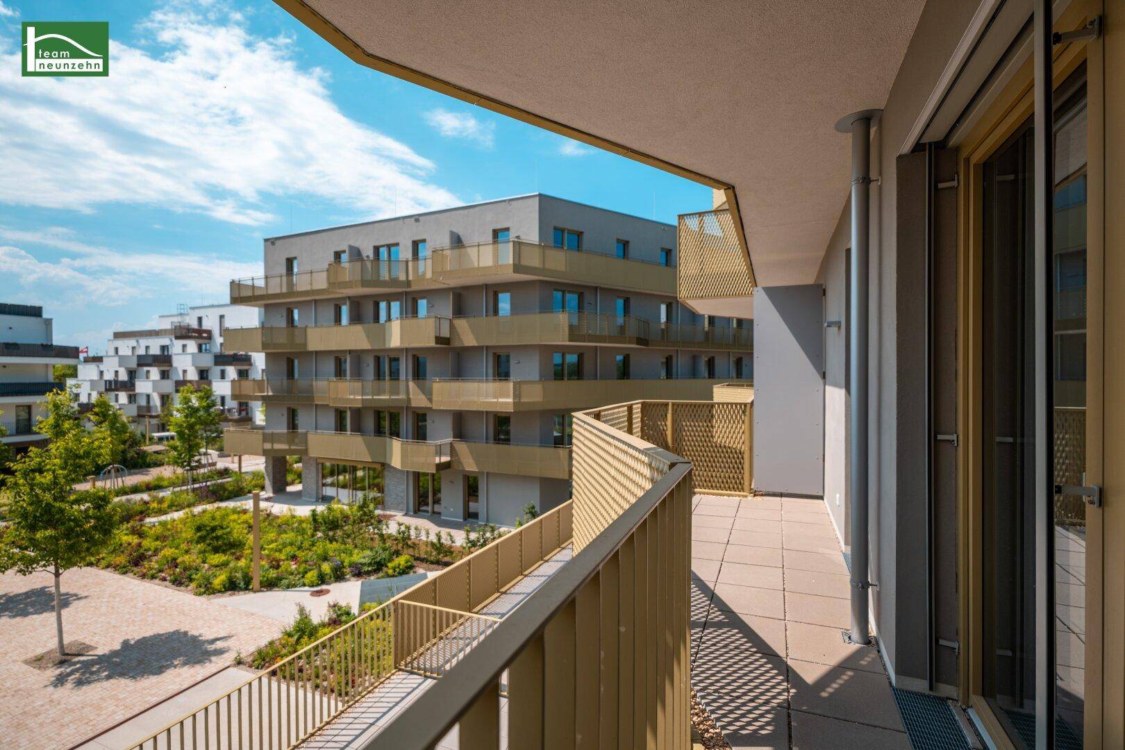 Blick vom Balkon auf die moderne Wohnanlage mit weiteren Gebäuden und gepflegten Grünflächen.