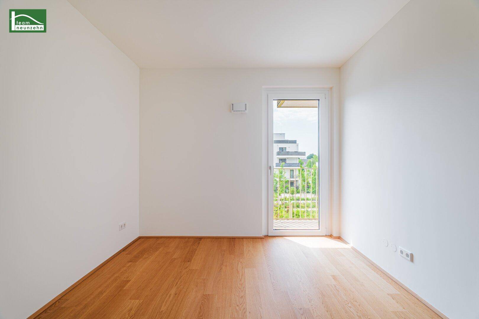 Heller Raum mit Holzboden und Zugang zu einem französischen Balkon mit Blick ins Grüne.