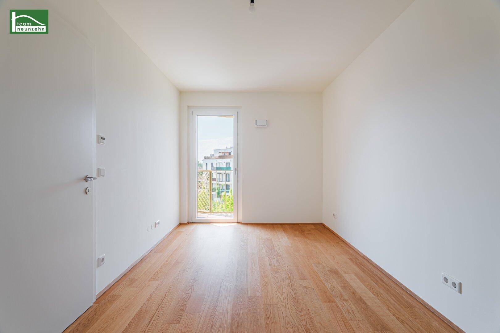Heller Raum mit Holzboden und Zugang zu einem kleinen Balkon, geeignet als Schlafzimmer.