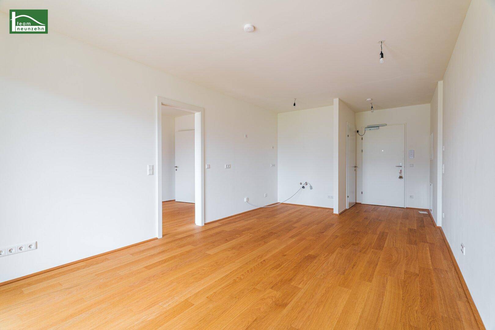 Geräumiger, heller Raum mit Holzparkett und weiß gestrichenen Wänden.