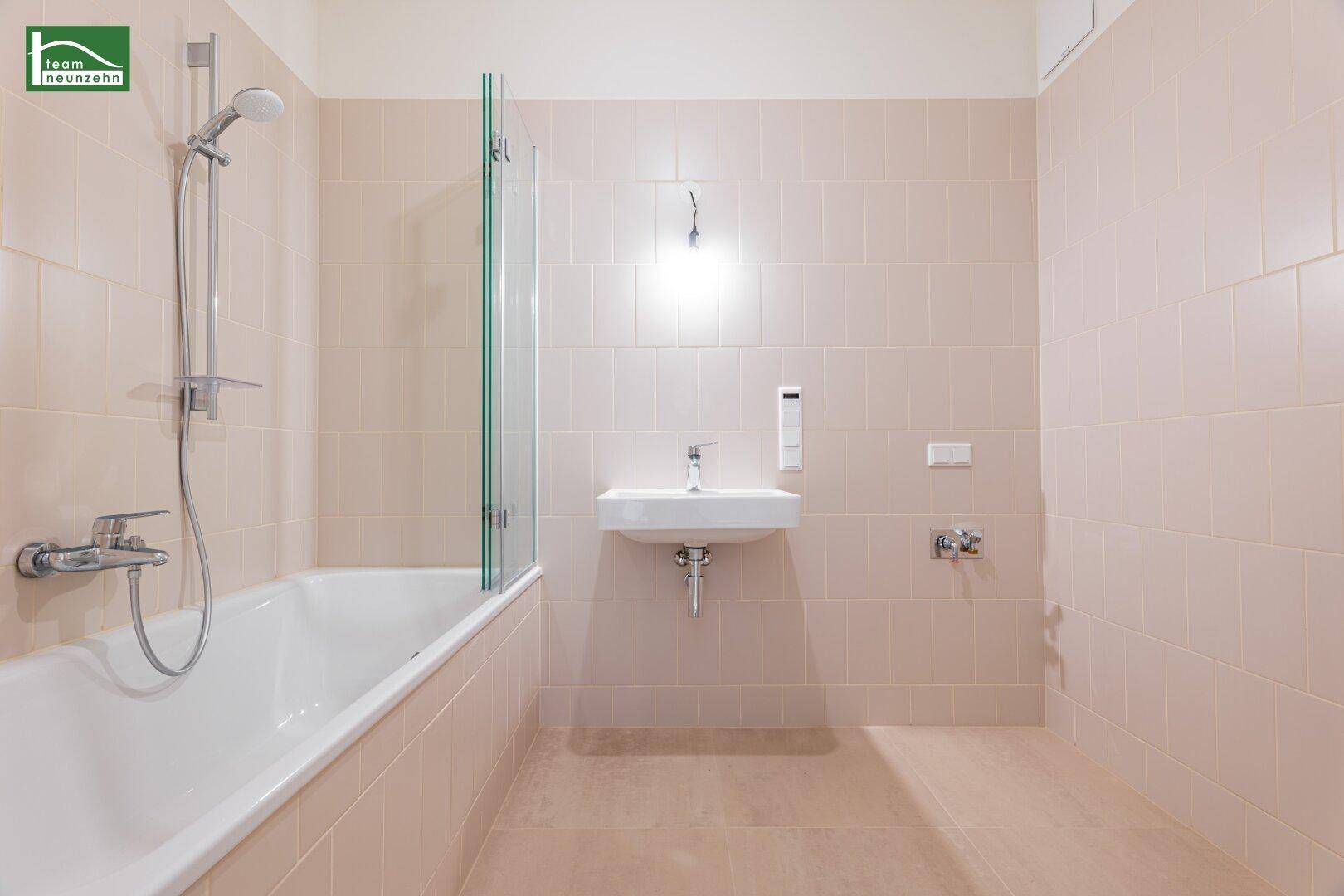 Helles Badezimmer mit Badewanne, Duschvorrichtung und beigefarbenen Wandfliesen.