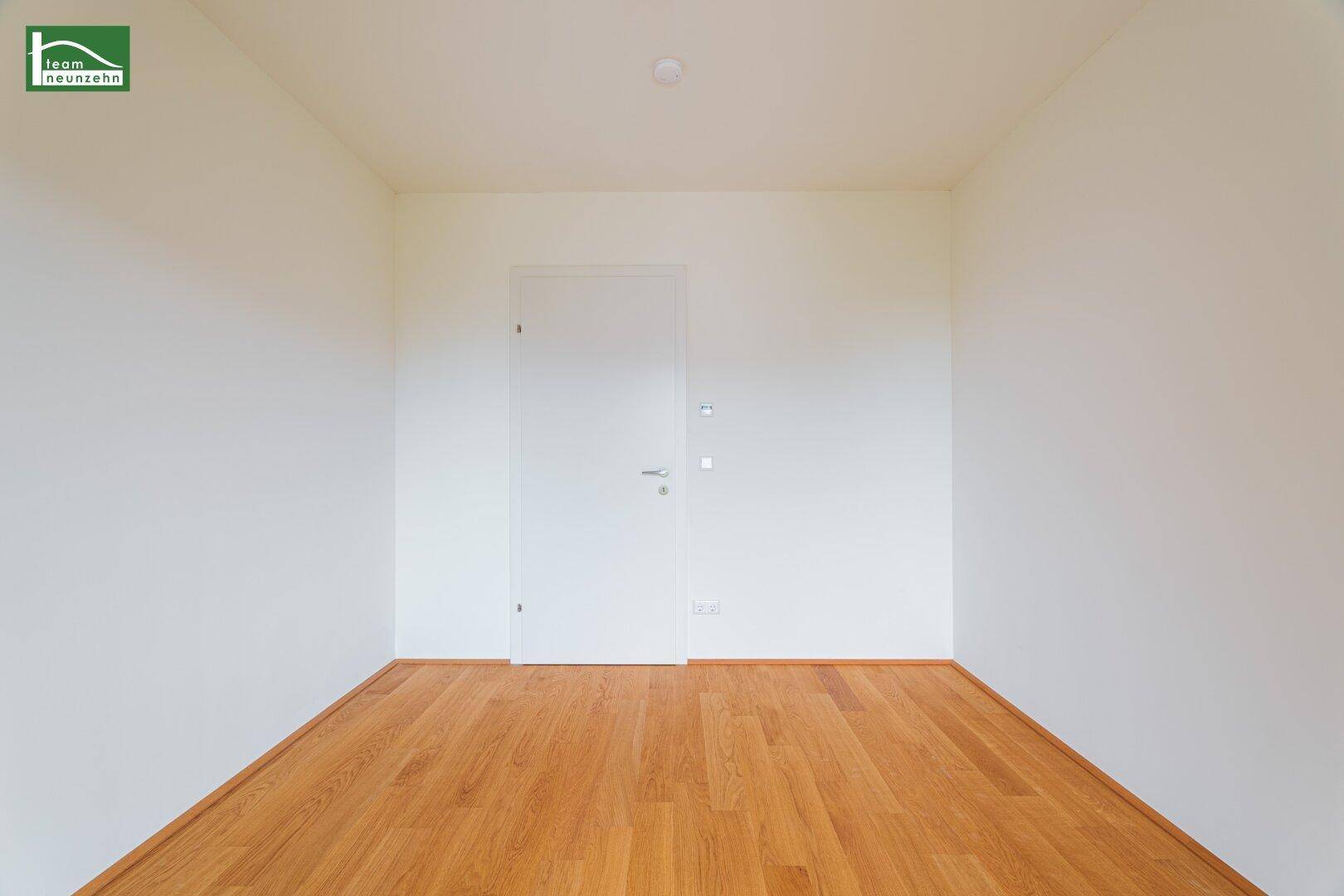 Leeres Zimmer mit Holzboden und weißer Tür, bereit für individuelle Gestaltung.