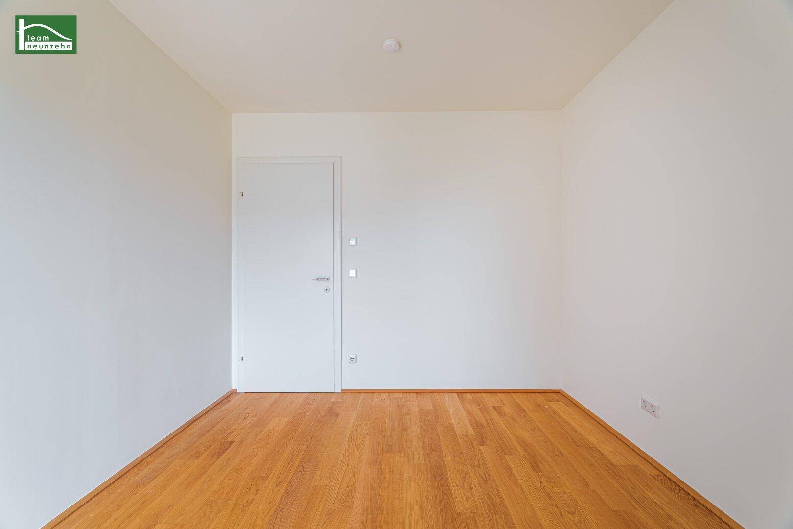 Leeres Zimmer mit Holzboden und weißer Tür, ideal für Schlaf- oder Arbeitszimmer.