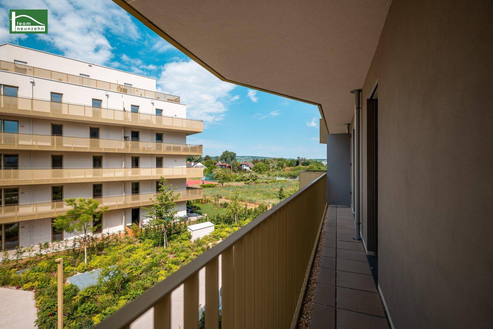 Langer Balkon mit seitlichem Blick auf die grüne Umgebung und weitere Gebäude.