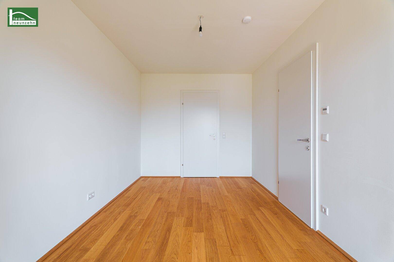 Helles, leeres Zimmer mit Holzboden und weißen Wänden, bereit zur Einrichtung.