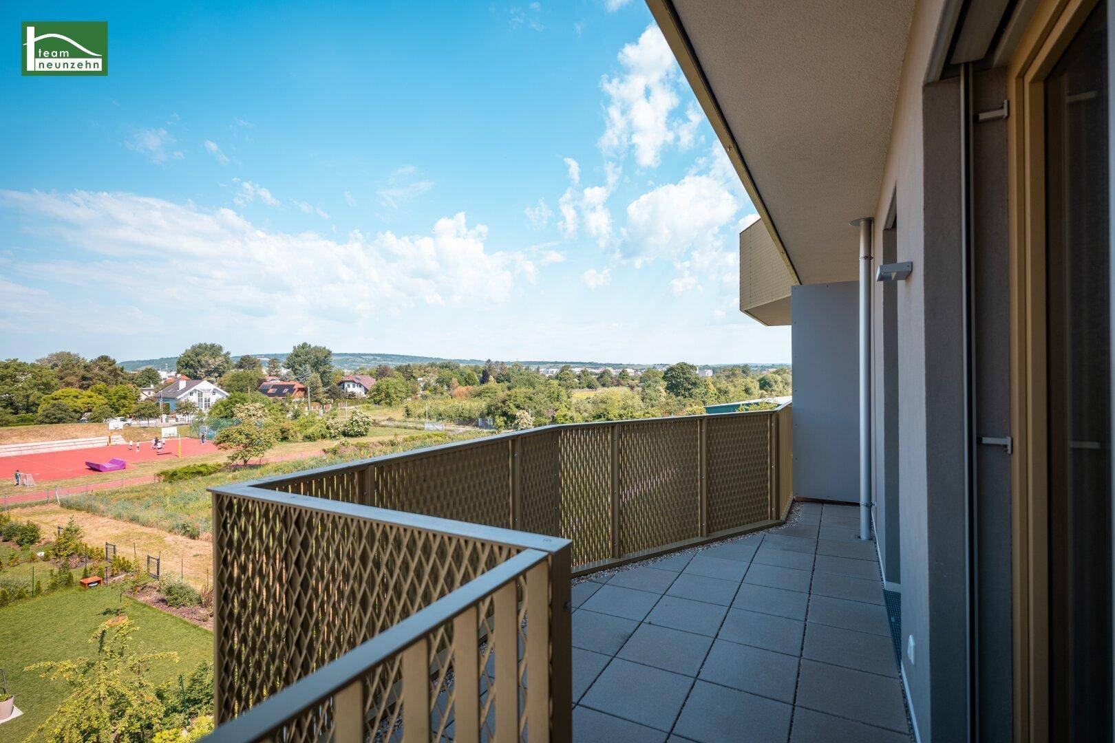Breiter Balkon mit Gittergeländer und weitem Blick über die grüne Umgebung.