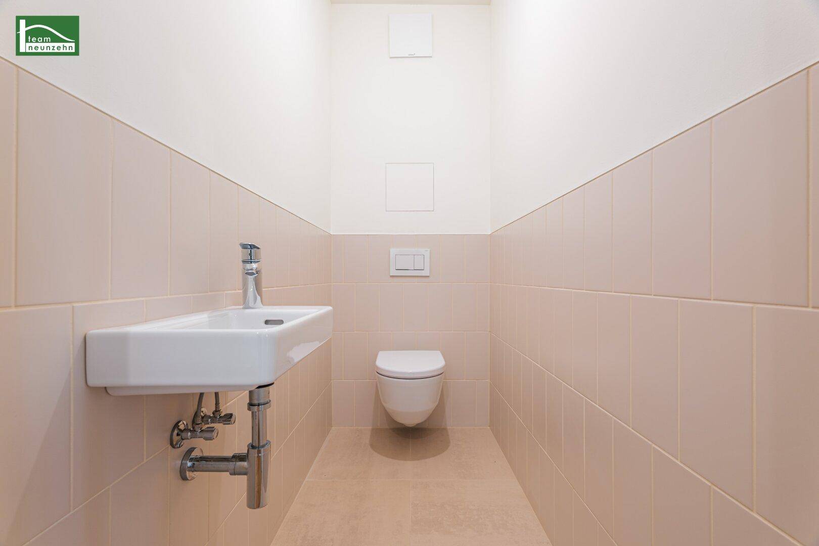 Gäste-WC mit beigefarbenen Fliesen, wandhängendem WC und modernem Waschbecken.
