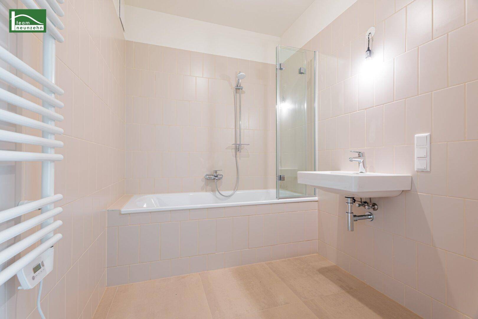 Modernes Badezimmer mit beigefarbenen Fliesen, Badewanne mit Duschwand und Handtuchheizkörper.