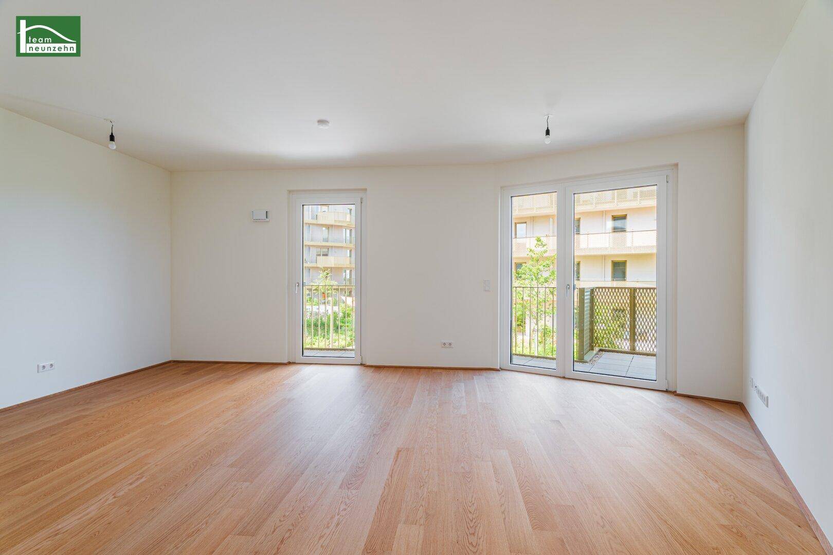 Helles, leeres Wohnzimmer mit hellem Laminatboden und Zugang zu einem Balkon.