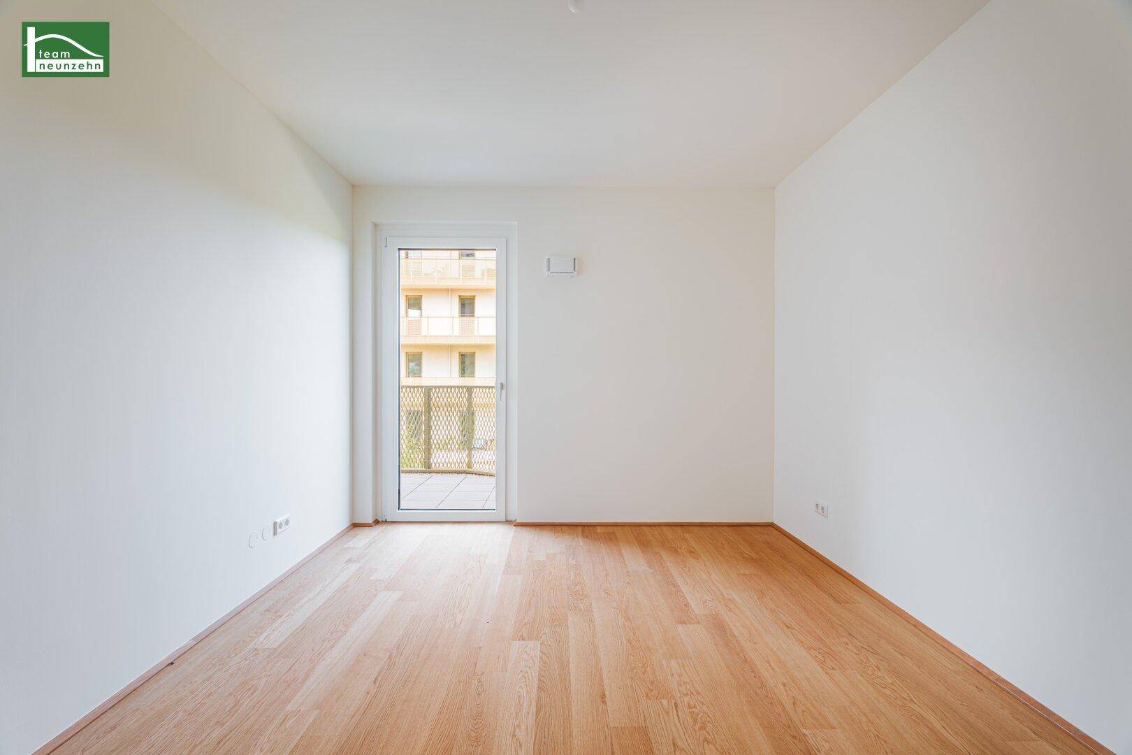 Leeres Zimmer mit Laminatboden, weißen Wänden und Zugang zu einem Außenbereich.