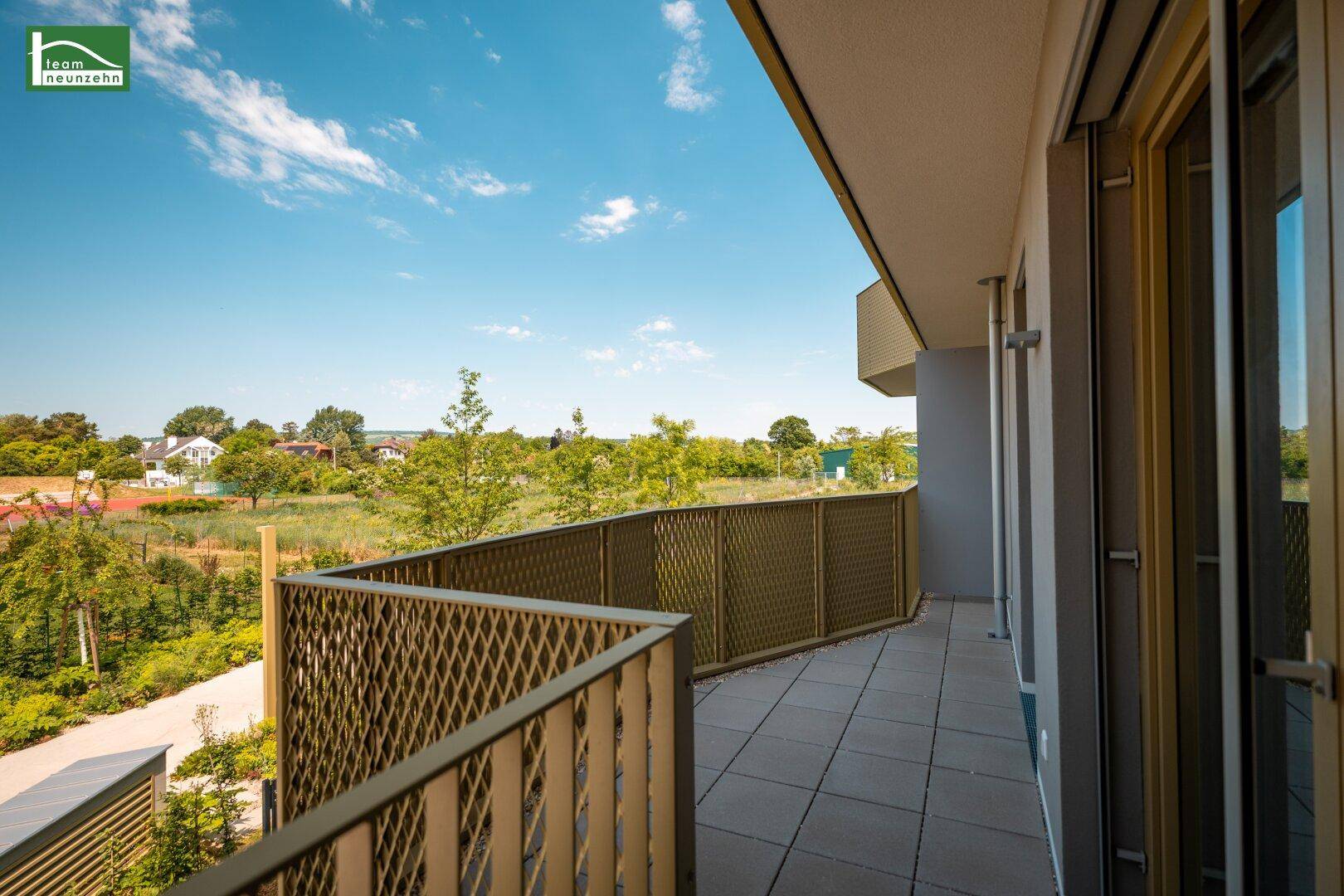 Breiter Balkon mit Fliesen und offener Aussicht auf die umliegende Natur und Wohnbebauung.