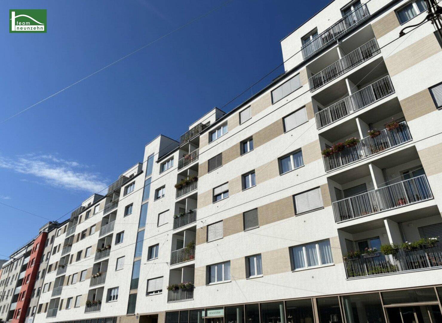 Moderne Wohngebäude mit zahlreichen Balkonen und großen Fenstern unter blauem Himmel.