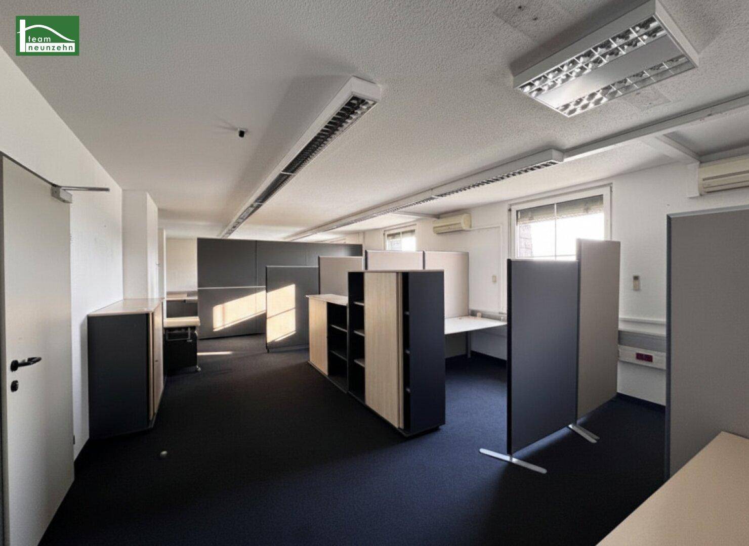 Großes Büro mit mehreren Arbeitsplätzen, Schränken und Trennwänden, gut beleuchtet.