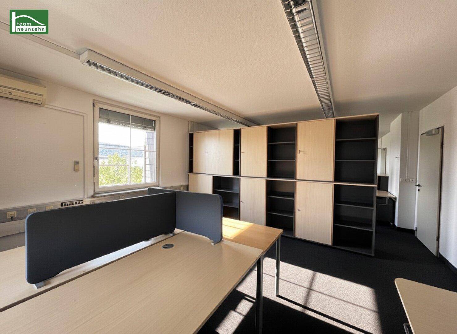 Bürofläche mit Schreibtischen, Trennwänden und integrierten Regalsystemen entlang der Wand.