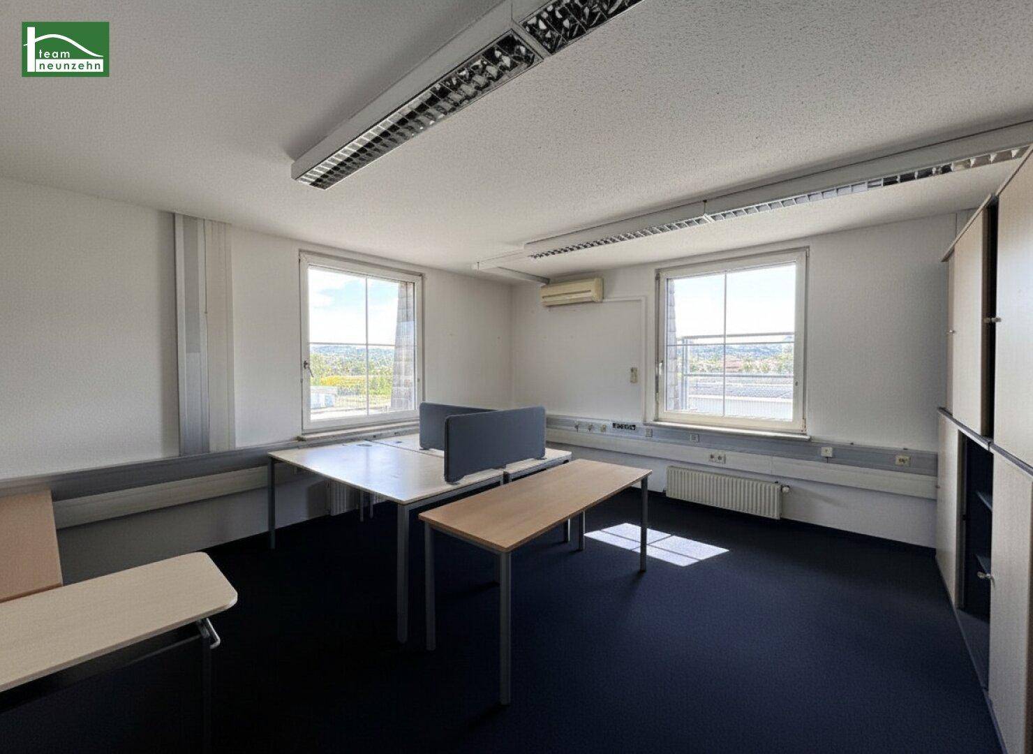 Helles Büro mit zwei Fenstern, Schreibtischen und Blick auf die Umgebung.