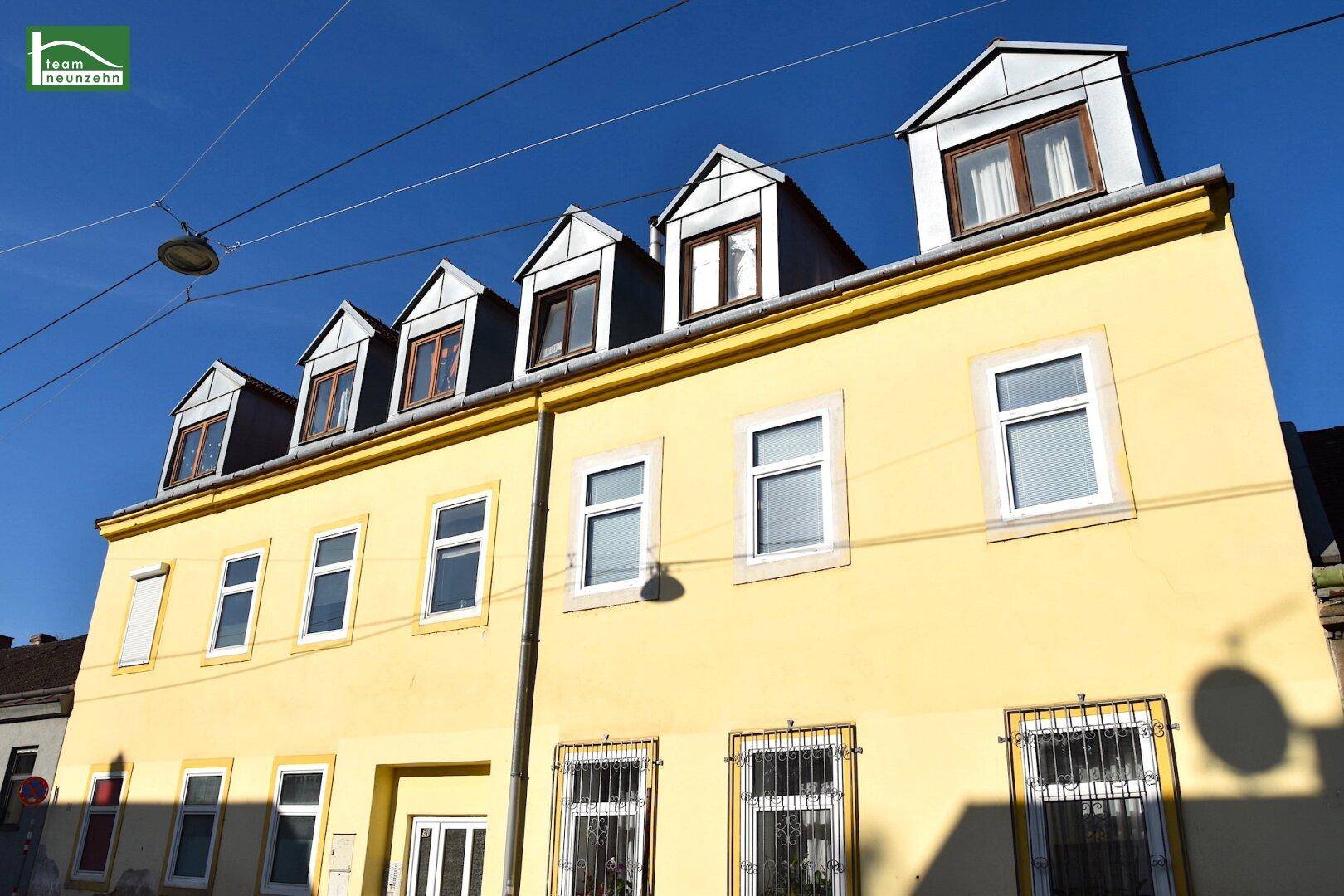 Gelbe Fassade eines gut erhaltenen Gebäudes mit großen Fenstern und Dachgauben im oberen Stockwerk.