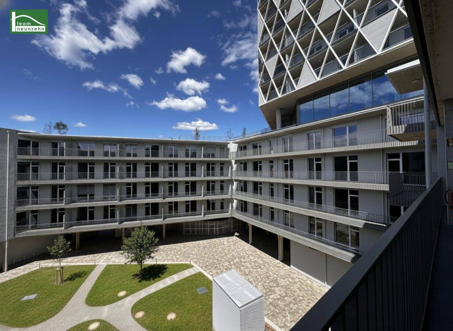 Moderner Gebäudekomplex mit geometrischer Fassade und begrüntem Innenhof unter blauem Himmel.