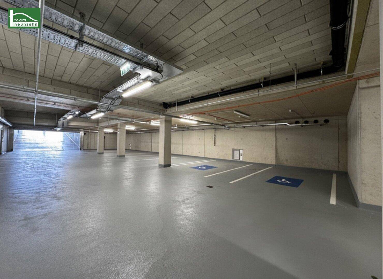 Tiefgarage mit markierten Behindertenparkplätzen und heller Beleuchtung in einem modernen Gebäude.