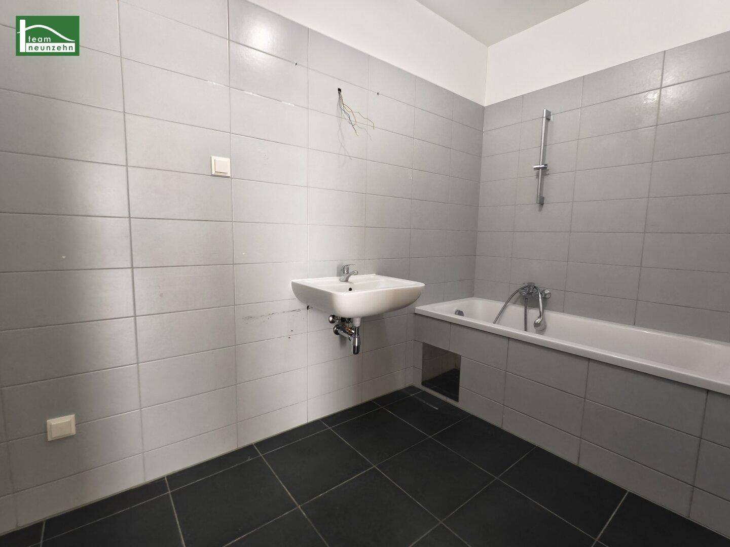 Modernes Badezimmer mit grauen Fliesen, Waschbecken und einer Badewanne.