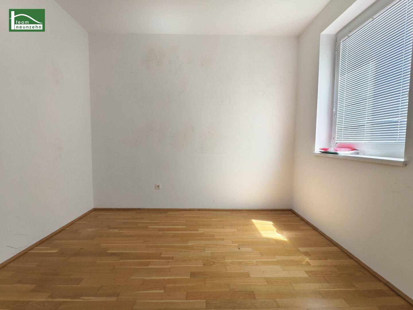 Helles Zimmer mit Parkettboden und Fenster, das viel natürliches Licht hereinlässt.
