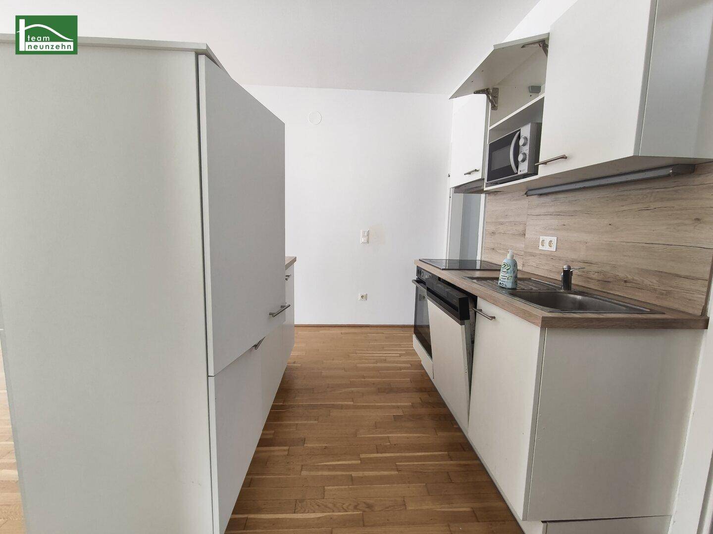 Moderne Küchenzeile mit weißen Schränken, Holzoptik-Arbeitsplatte und integrierten Geräten.