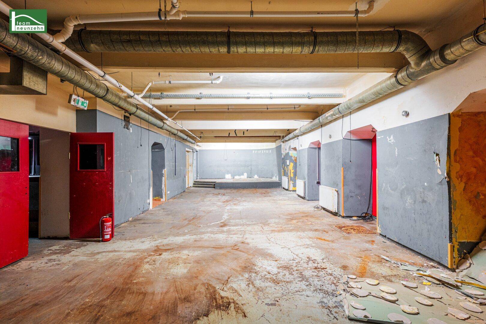 Großer, leerer Gewerberaum im Untergeschoss mit sichtbaren Rohren und abgenutztem Betonboden.
