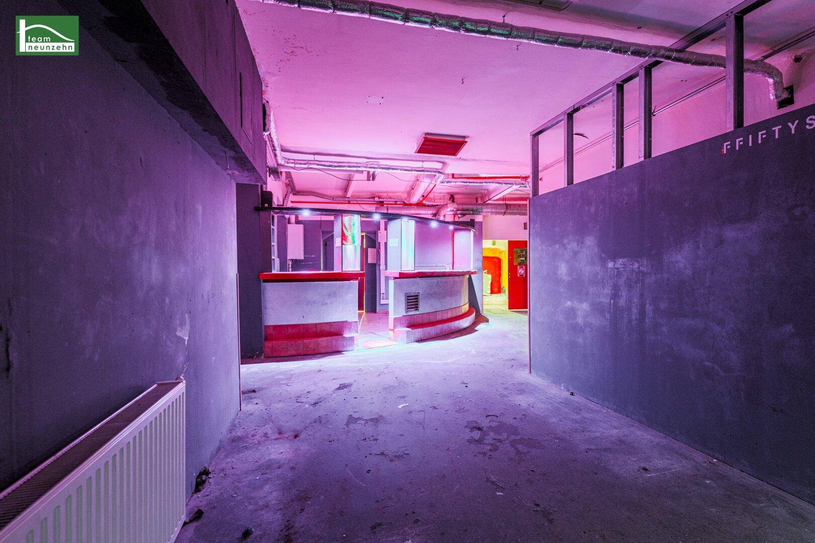 Großer Gewerberaum mit Bar, lila Beleuchtung und sichtbaren Rohren, bereit für eine Neugestaltung.