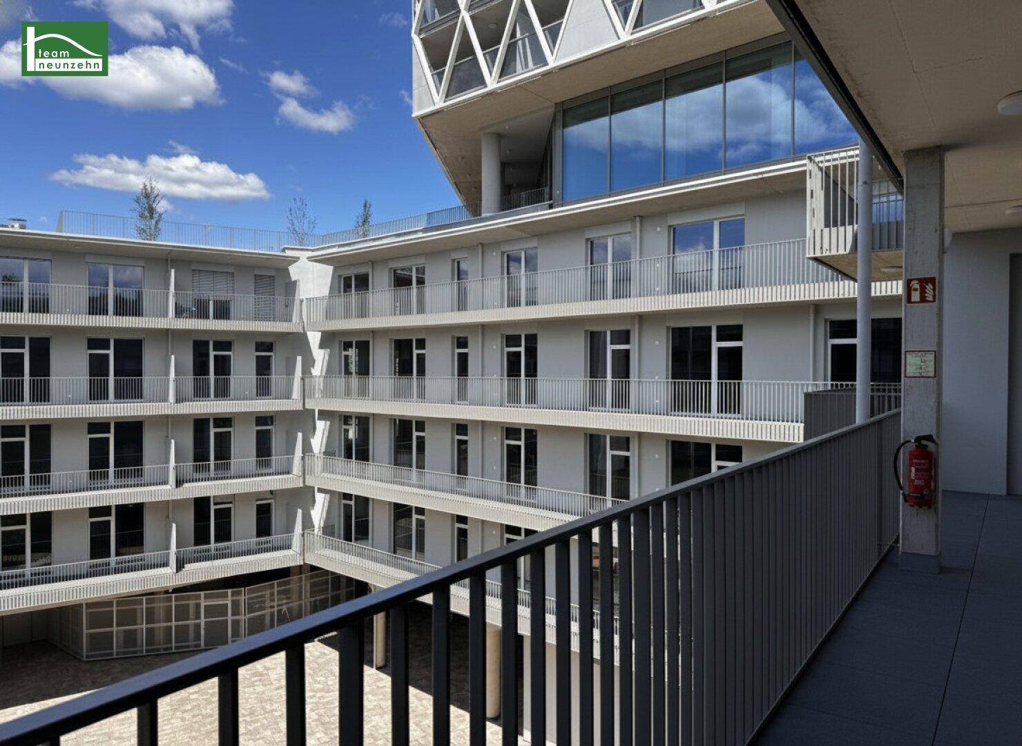 Blick von einem Balkon auf den Innenhof eines modernen Apartmentkomplexes mit weiteren Balkonen.