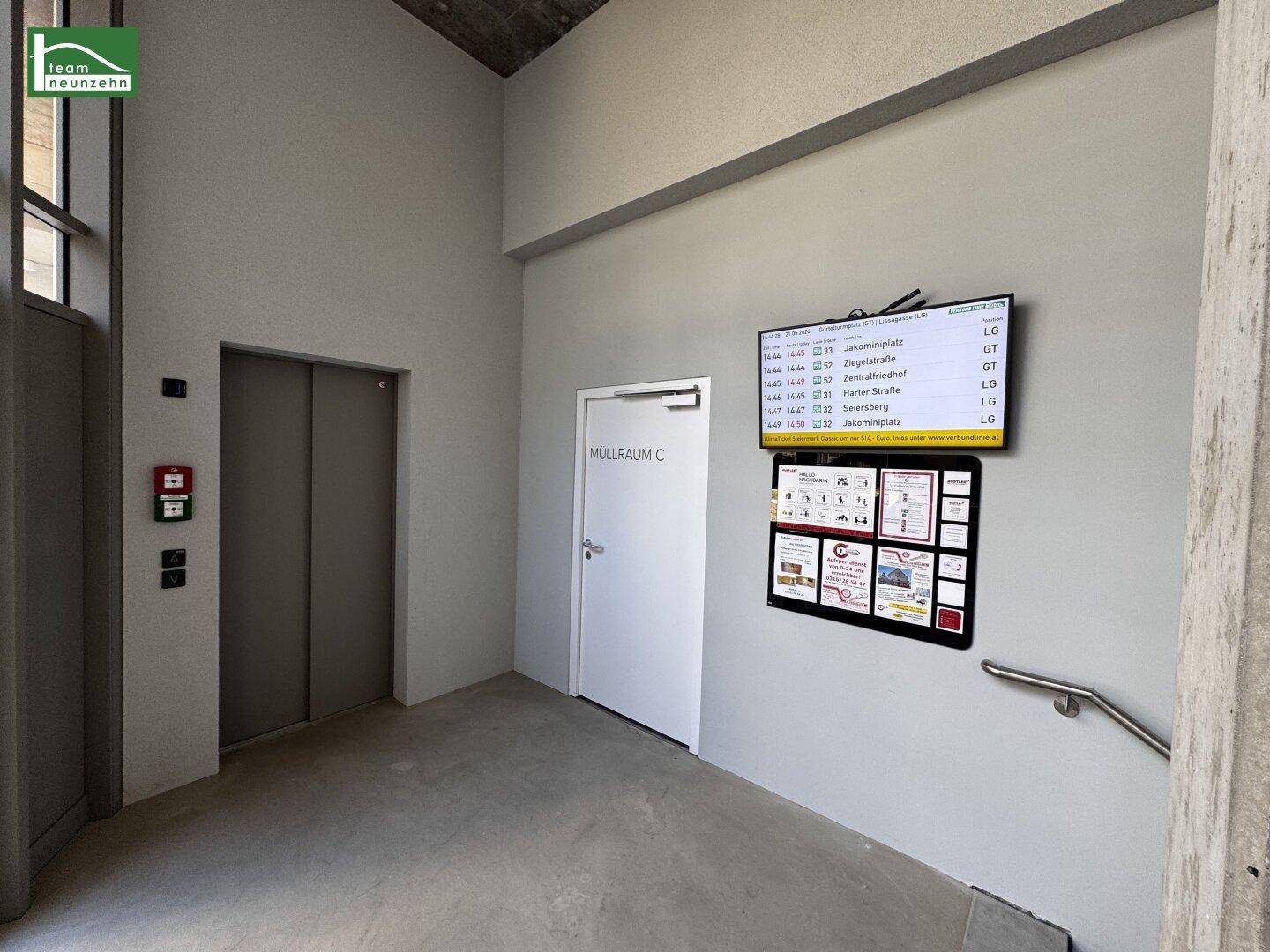 Moderner Flurbereich mit Aufzug, Müllraumzugang und digitalen Informationsanzeigen.