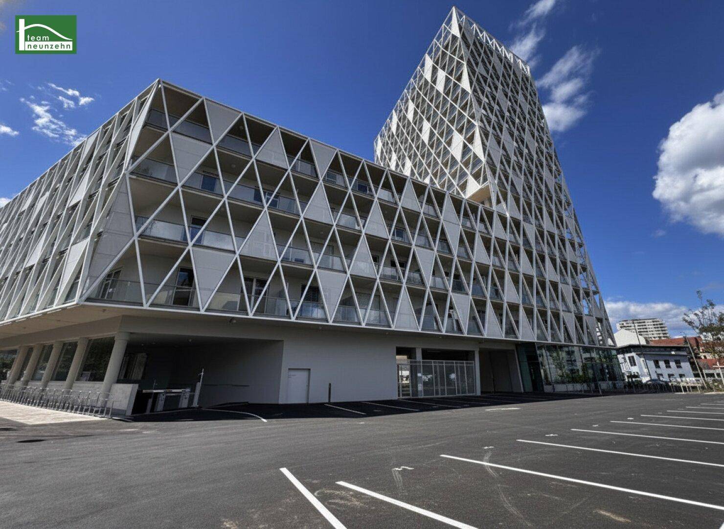 Moderne Architektur mit markanter geometrischer Fassade und großem Parkplatz.