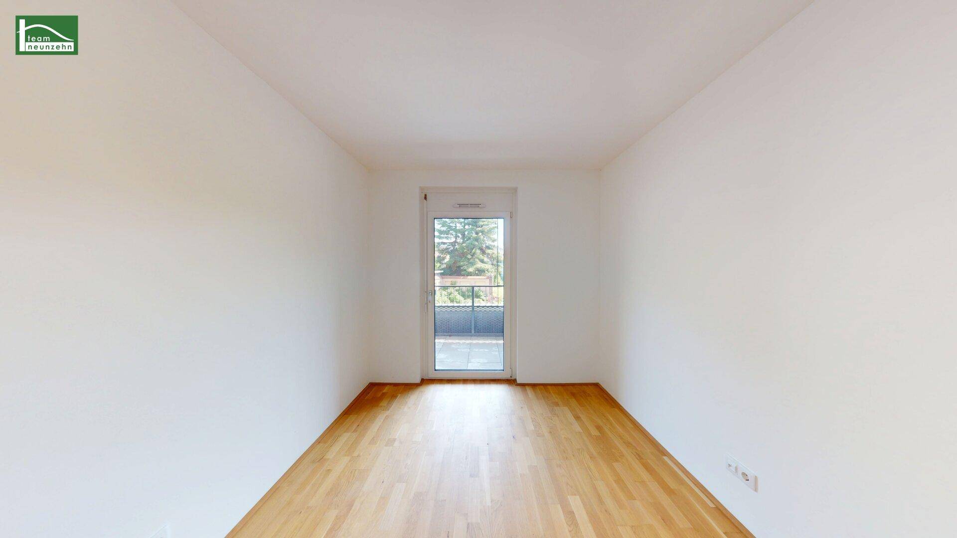 Leeres Schlafzimmer mit Holzboden und Fenstertür, die zu einem französischen Balkon führt.