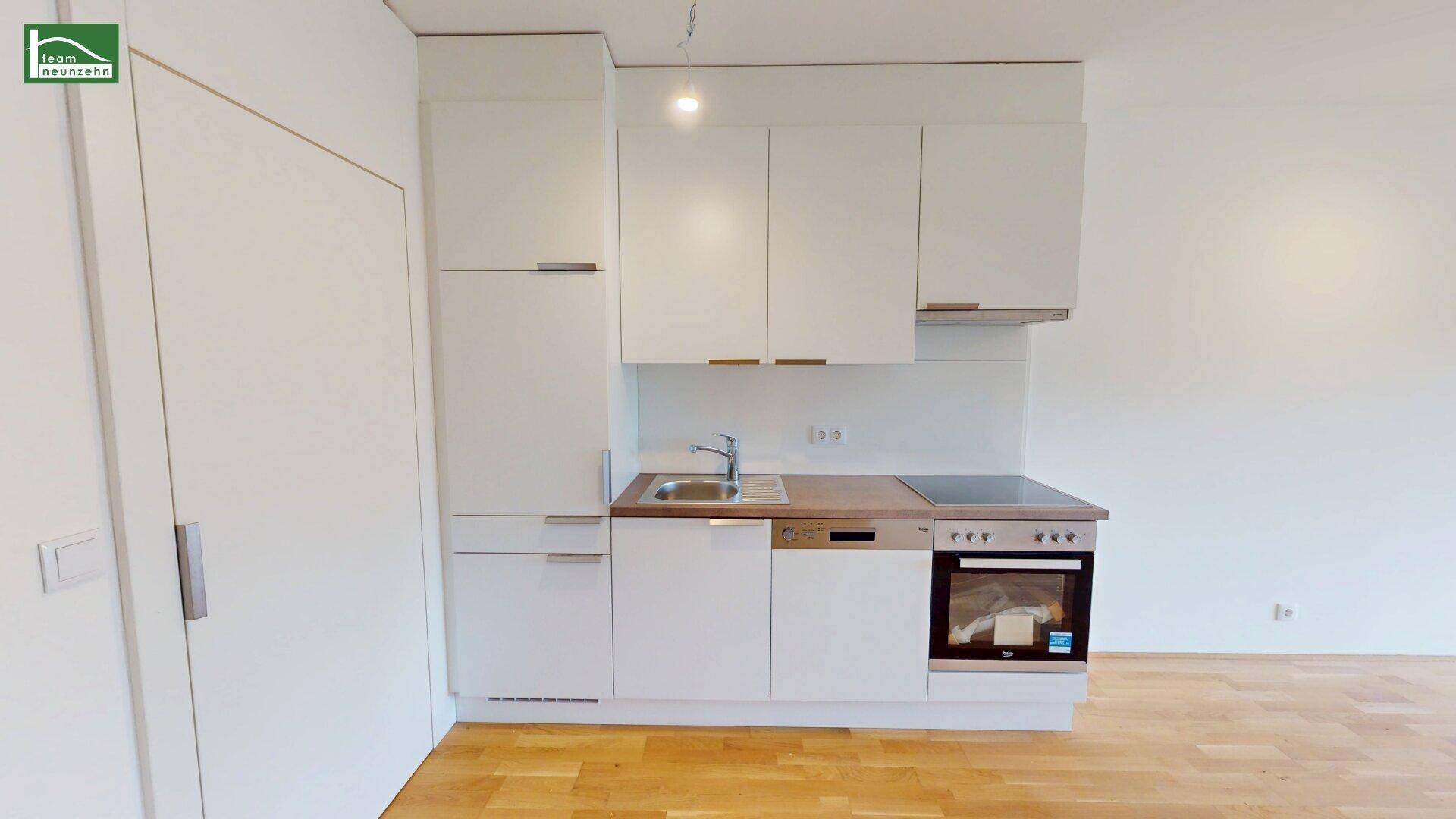 Kompakte Einbauküche mit weißen Fronten, integrierten Geräten und einer Arbeitsplatte in Holzoptik.