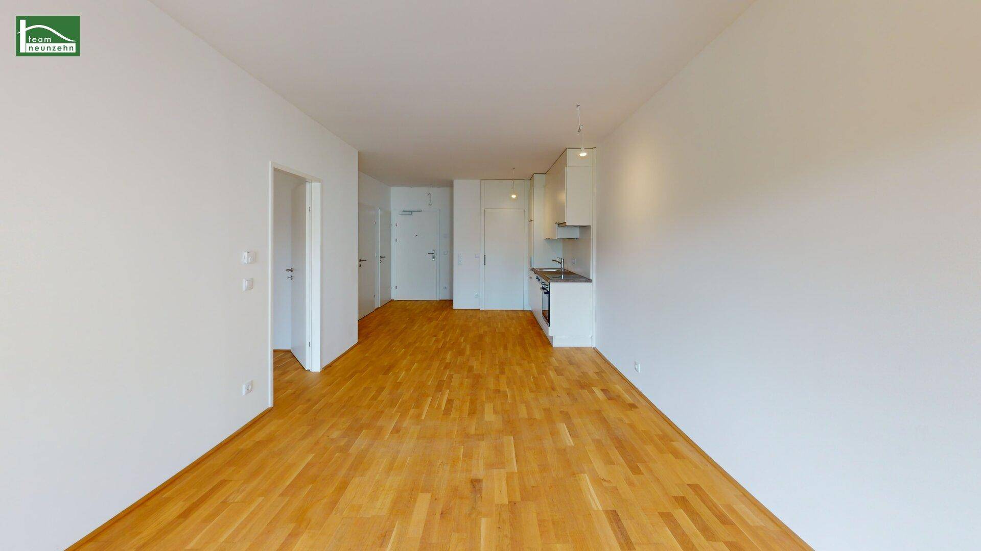 Heller Wohnbereich mit Holzboden und integrierter Küchenzeile in modernem, unmöbliertem Zustand.