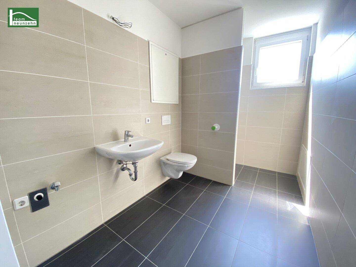 Helles Badezimmer mit beigen Wandfliesen, dunklem Boden und wandhängendem WC.